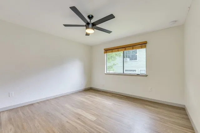 an empty room with wooden floor ceiling fan and windows