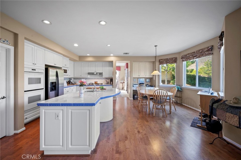 3262 Bluebird Circle Simi Valley, CA 93063 - Photo 12 of 43 a kitchen with stainless steel appliances granite countertop a stove top oven a refrigerator a dining table and chairs with wooden floor