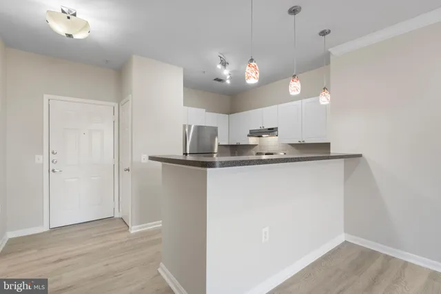 an empty room with wooden floor and kitchen view