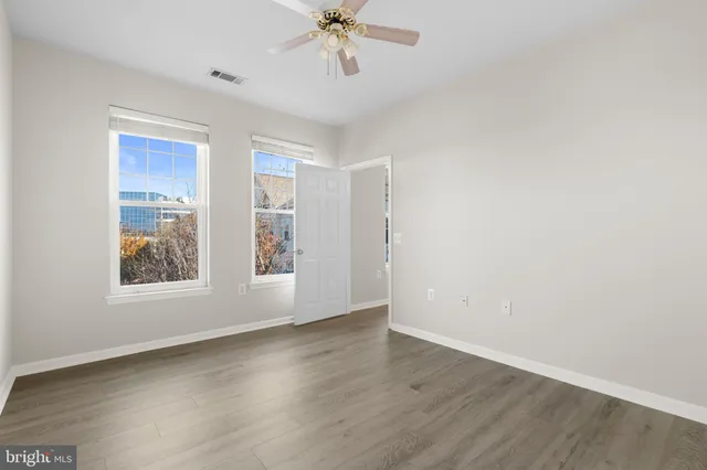 an empty room with wooden floor chandelier fan and windows