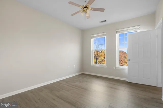an empty room with wooden floor fan and windows