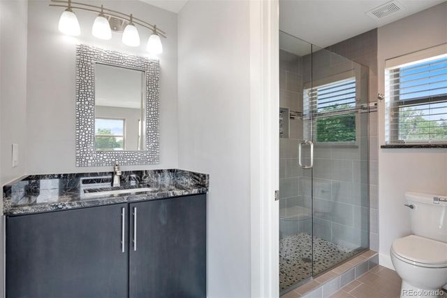 a bathroom with a granite countertop sink a toilet a mirror and shower