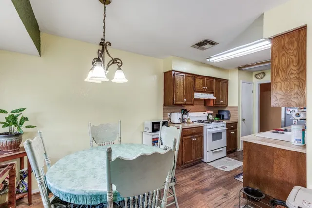 a kitchen with stainless steel appliances granite countertop a stove a refrigerator a kitchen island a dining table and chairs with wooden floor