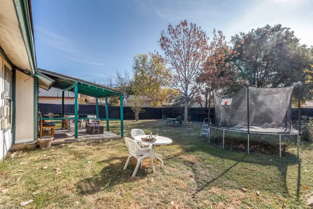 a view of a patio with a table and chairs under an umbrella with large trees