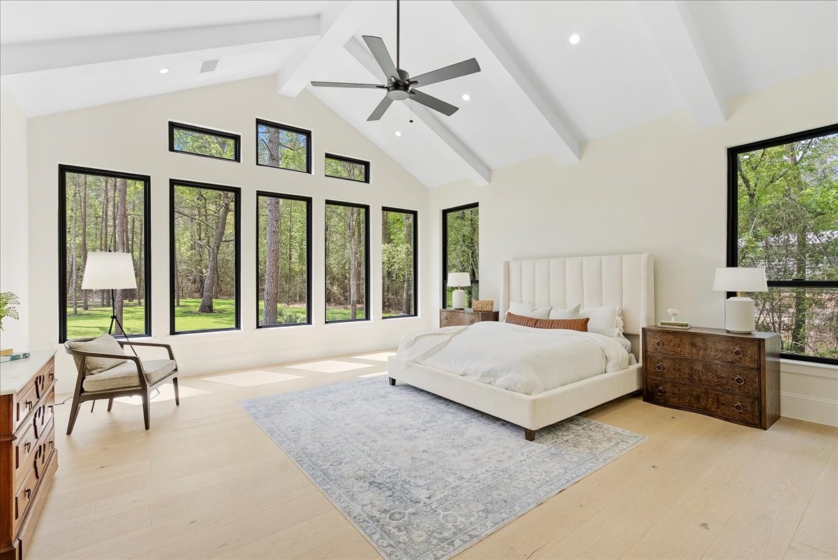 26041 Crown Ranch Boulevard Montgomery, TX 77316 - Photo 31 of 45 Cathedral ceilings with exposed wood beams and walls of windows give the primary suite a grand sense of scale while keeping the space warm, peaceful, and connected to the surrounding pines.