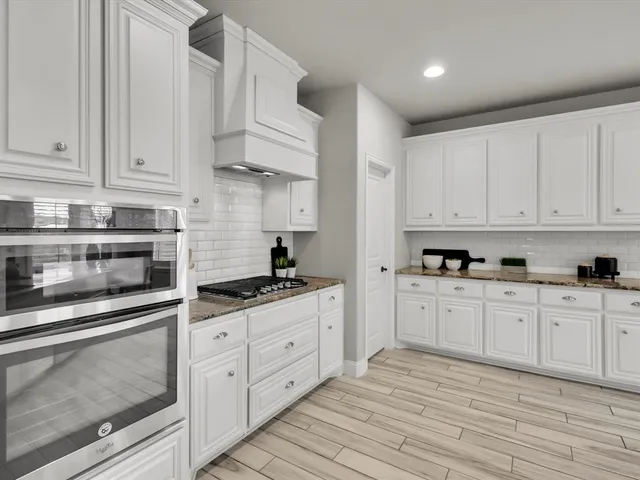 a large white kitchen with wooden floor and stainless steel appliances