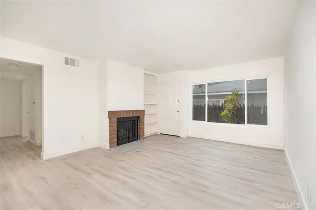 an empty room with wooden floor fireplace and windows