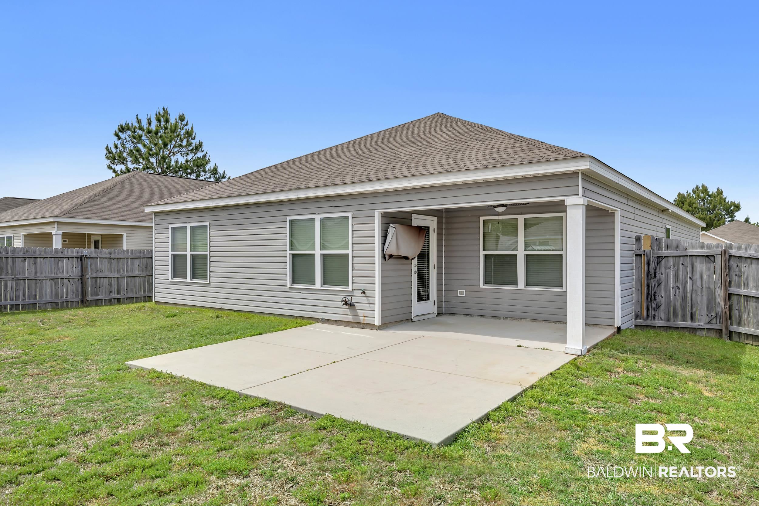17344 Harding Drive Foley, AL 36535 - Photo 32 of 46 Spacious backyard featuring a gray vinyl-sided exterior, a covered patio area with a light-colored concrete slab, a separate concrete patio extension, multiple windows, and a wood privacy fence