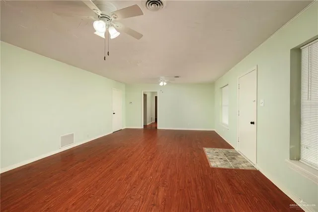 a view of an empty room with wooden floor and a ceiling fan
