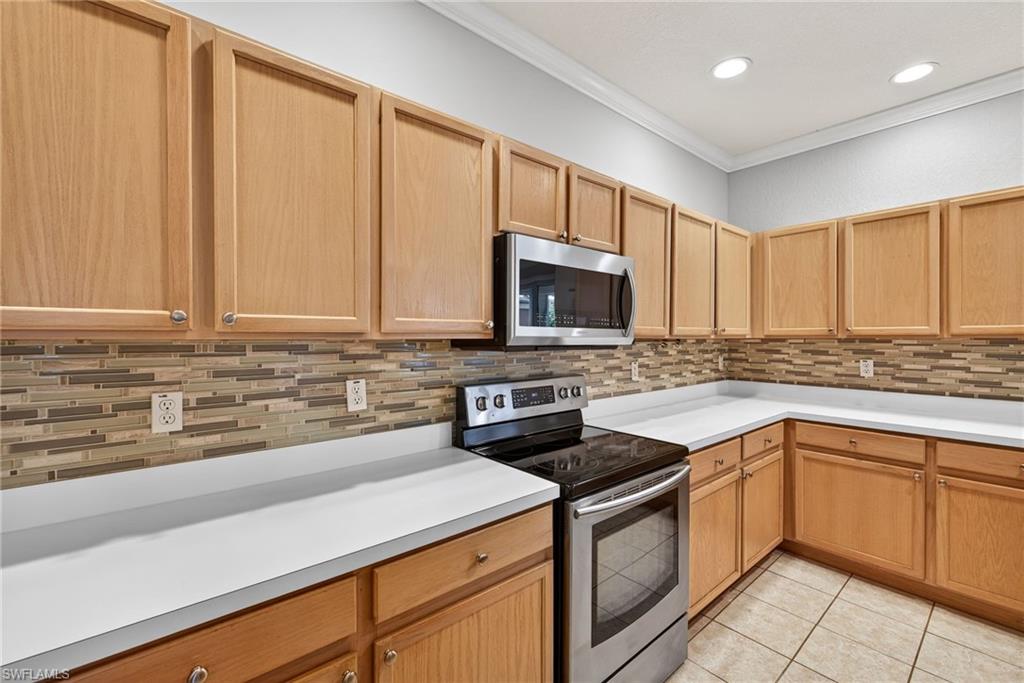 599 Crossfield Circle, Unit 35 Naples, FL 34104 - Photo 11 of 26 Kitchen with stainless steel appliances, light countertops, crown molding, light tile patterned floors, and decorative backsplash