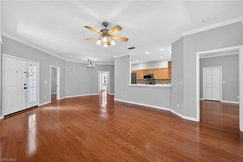 599 Crossfield Circle, Unit 35 Naples, FL 34104 - Photo 4 of 26 Unfurnished living room featuring dark wood finished floors, crown molding, a ceiling fan, and suspended lighting