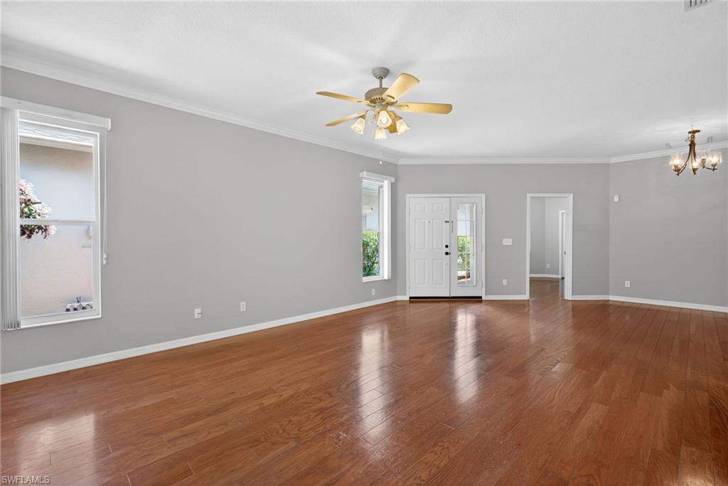 599 Crossfield Circle, Unit 35 Naples, FL 34104 - Photo 9 of 26 Unfurnished living room featuring dark wood finished floors, a ceiling fan, crown molding, and a chandelier