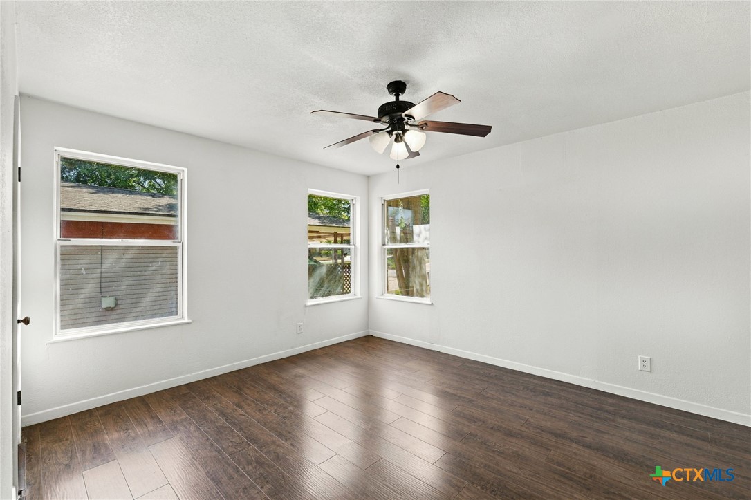 904 Kirk Street Taylor, TX 76574 - Photo 13 of 25 Primary Bedroom Retreat showing three windows, fresh paint, recent flooring update, & a ceiling fan.