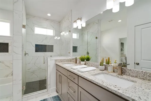 a bathroom with a granite countertop double vanity sink mirror and shower