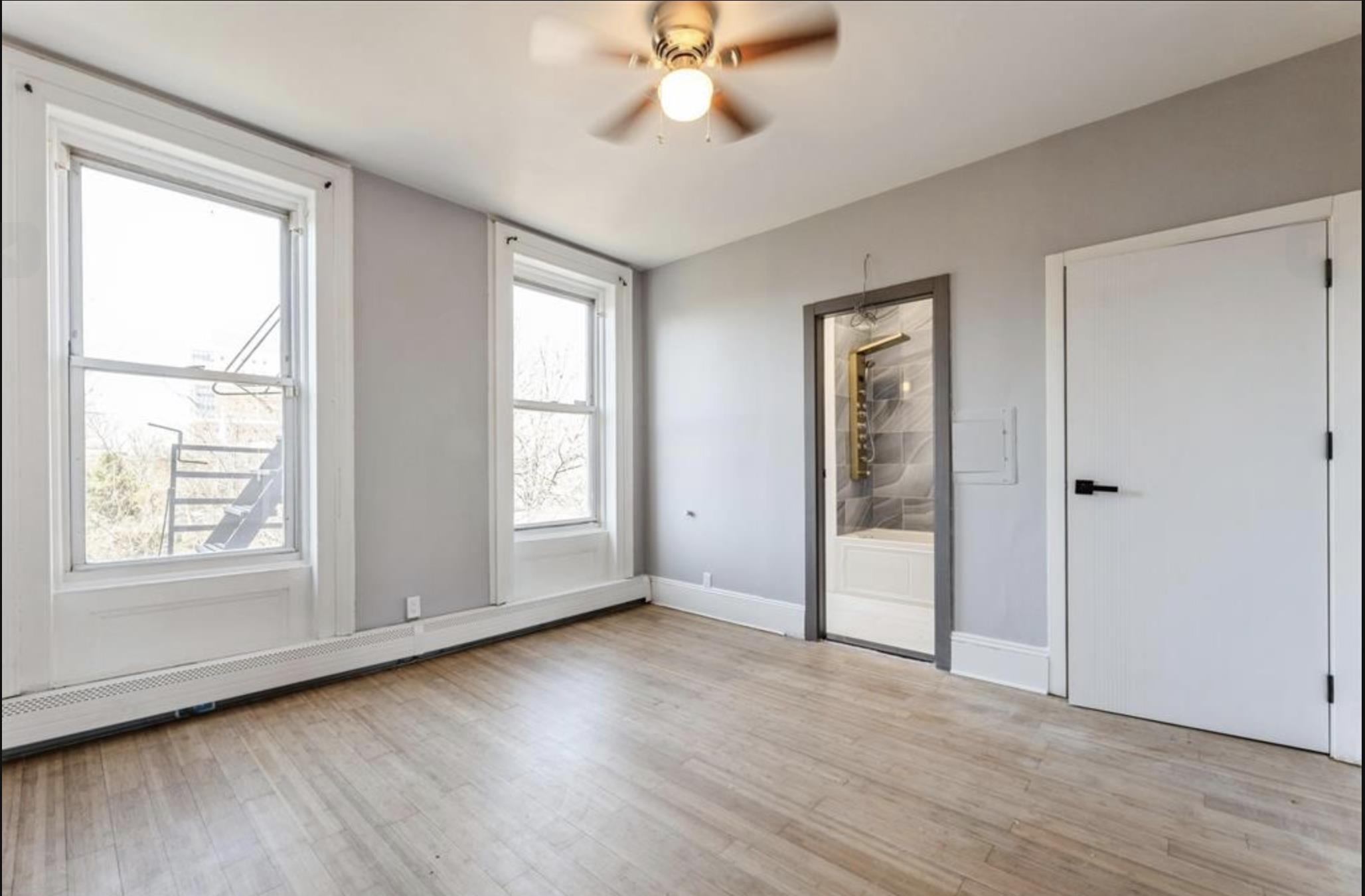 an empty room with wooden floor chandelier fan and windows