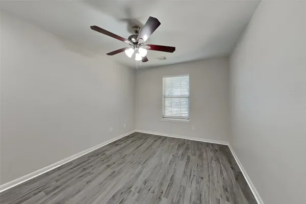 an empty room with wooden floor fan and windows