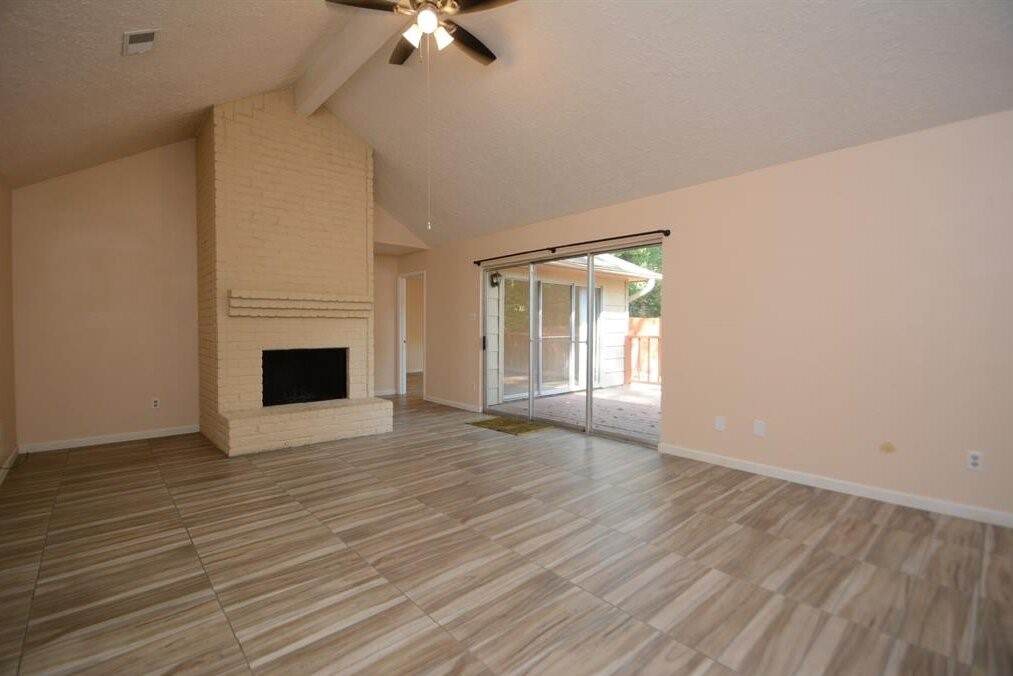 15 South Tallowberry Drive Spring, TX 77381 - Photo 5 of 26 Spacious living room with vaulted ceilings, brick fireplace, tile flooring, and large sliding glass doors for abundant natural light.