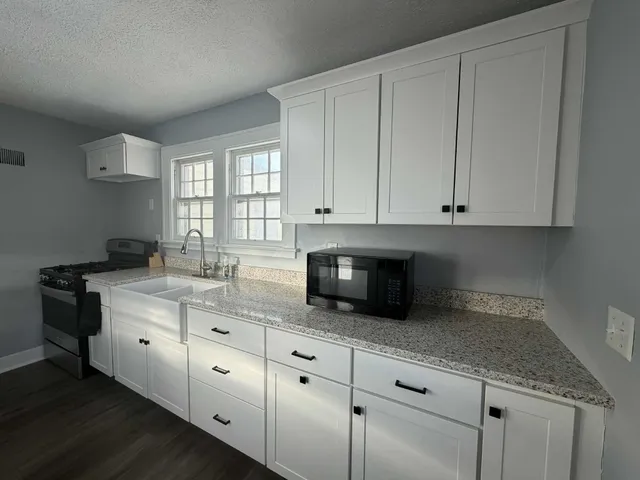 a kitchen with granite countertop white cabinets stainless steel appliances a sink and a window