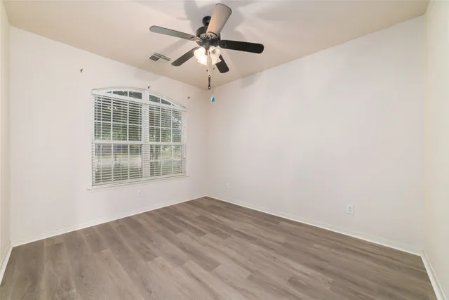 an empty room with wooden floor fan and windows