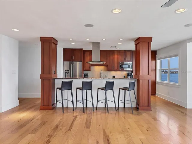 a kitchen with stainless steel appliances kitchen island granite countertop a dining table chairs and a refrigerator