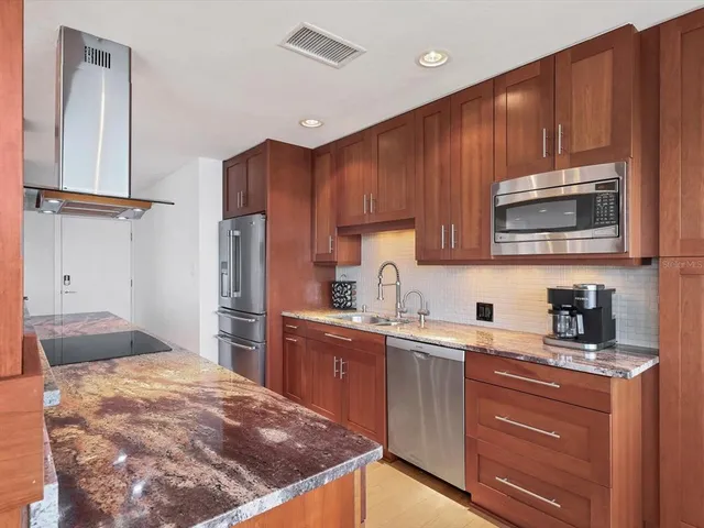 a kitchen with kitchen island granite countertop wooden cabinets stainless steel appliances and a sink