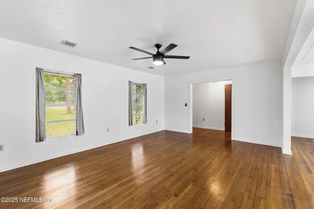 a view of an empty room with window and wooden floor