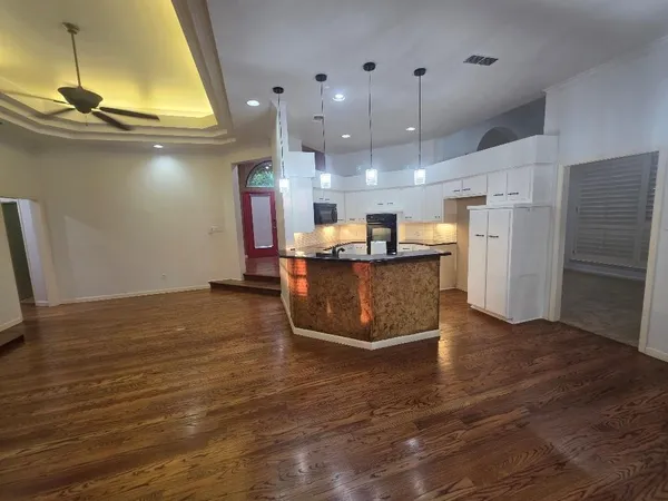 a room with stainless steel appliances kitchen island granite countertop a refrigerator a stove and a wooden floors
