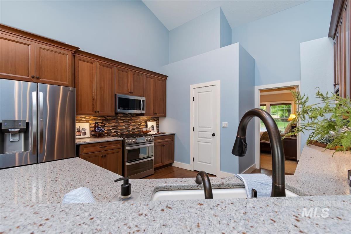 10462 West Lanktree Gulch Road Star, ID 83669 - Photo 15 of 48 Kitchen featuring a speckled countertop, brown wood cabinetry, stainless steel appliances, a multi-toned backsplash, and vaulted ceilings