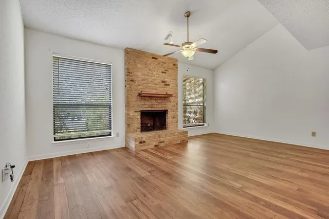 a view of an empty room with wooden floor fireplace and a window