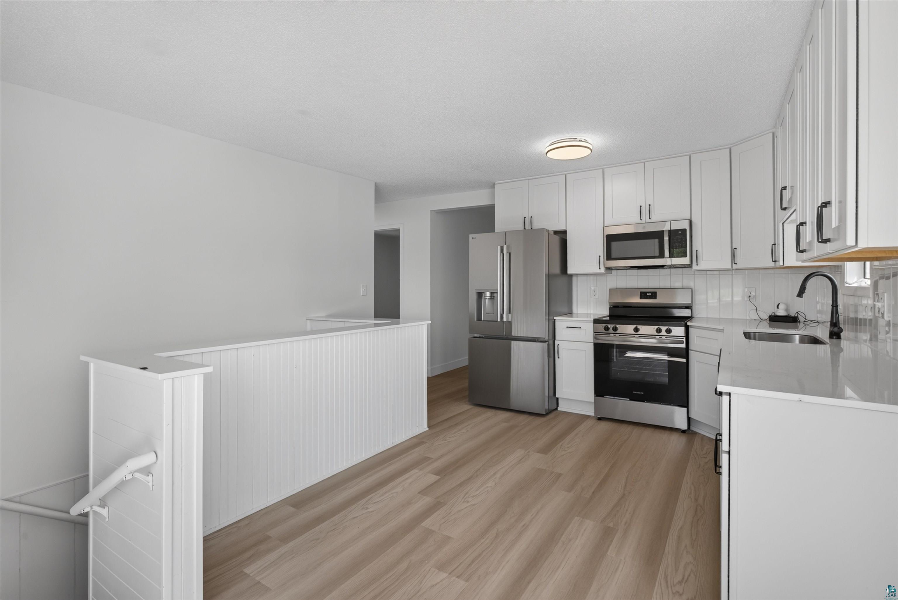 5868 Rice Lake Road Duluth, MN 55803 - Photo 13 of 39 Bright kitchen featuring stainless steel appliances, white cabinetry, a subway tile backsplash, and light-toned wood-finish flooring