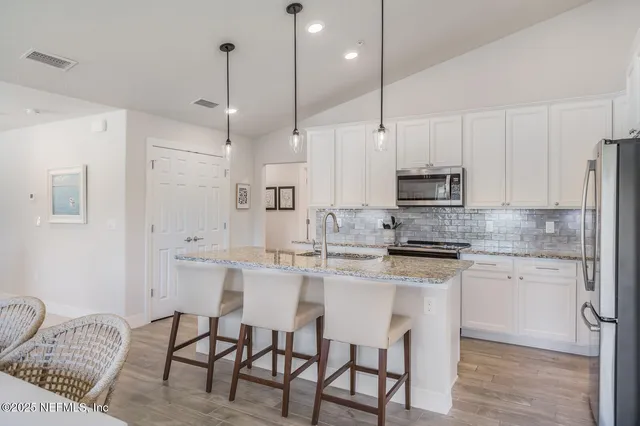 a kitchen with stainless steel appliances kitchen island granite countertop a sink a stove a refrigerator and white cabinets with wooden floor