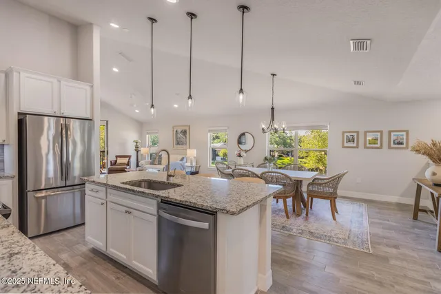 a kitchen with stainless steel appliances granite countertop a sink a refrigerator a stove a dining table chairs and kitchen view