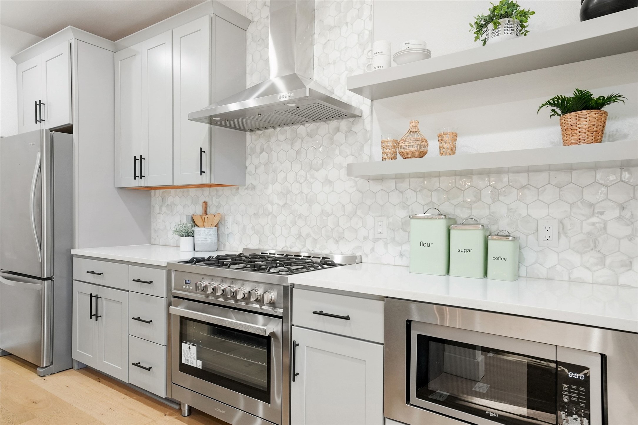 5109 Stone Gate Drive, Unit 2 Austin, TX 78721 - Photo 4 of 23 Kitchen featuring stainless steel appliances, wall chimney exhaust hood, open shelves, light wood-type flooring, and white cabinets