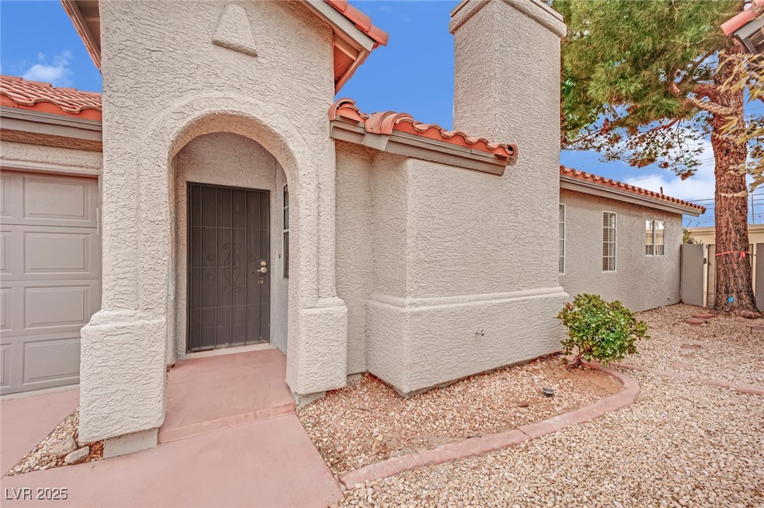 Doorway to property featuring a tiled roof, a chimney, and stucco siding