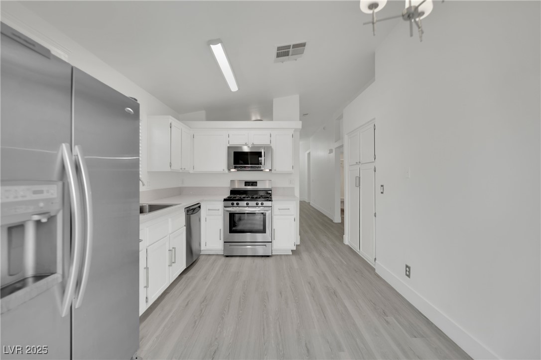 2218 Ramsgate Drive Henderson, NV 89074 - Photo 21 of 33 Kitchen featuring light wood finished floors, visible vents, stainless steel appliances, light countertops, and white cabinetry