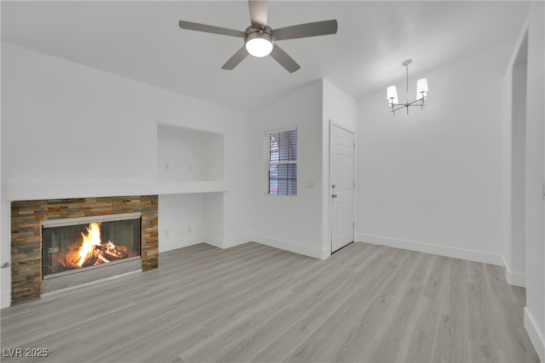 2218 Ramsgate Drive Henderson, NV 89074 - Photo 31 of 33 Unfurnished living room featuring a glass covered fireplace, light wood-style flooring, baseboards, and ceiling fan with notable chandelier