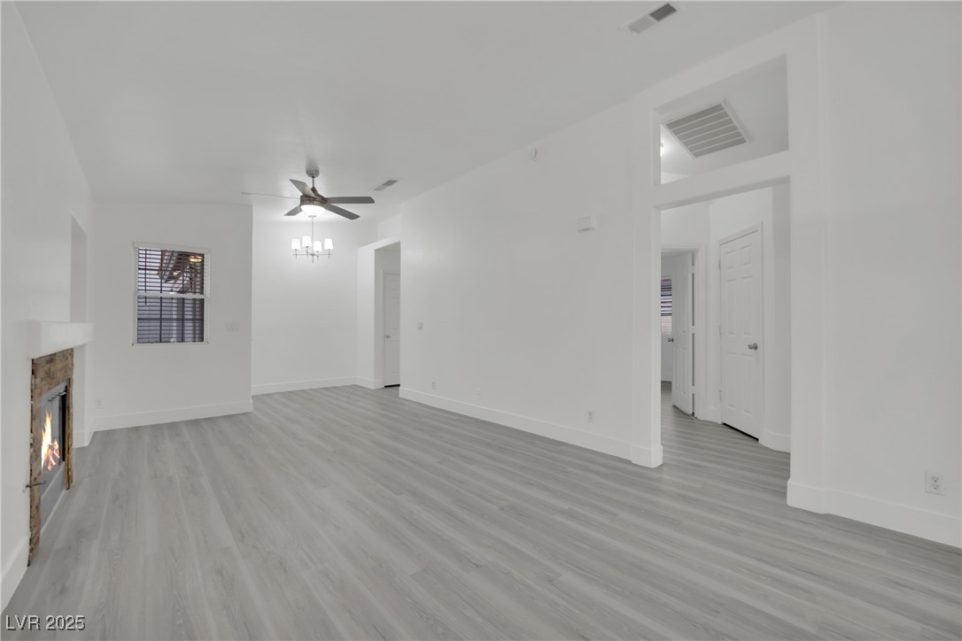 2218 Ramsgate Drive Henderson, NV 89074 - Photo 4 of 33 Unfurnished living room featuring a lit fireplace, visible vents, light wood-style flooring, and a ceiling fan