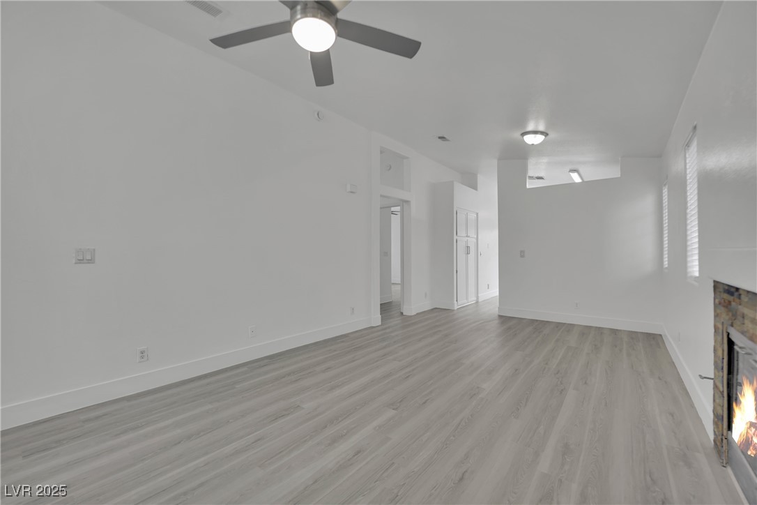 2218 Ramsgate Drive Henderson, NV 89074 - Photo 8 of 33 Unfurnished living room featuring ceiling fan, visible vents, baseboards, light wood-type flooring, and a glass covered fireplace