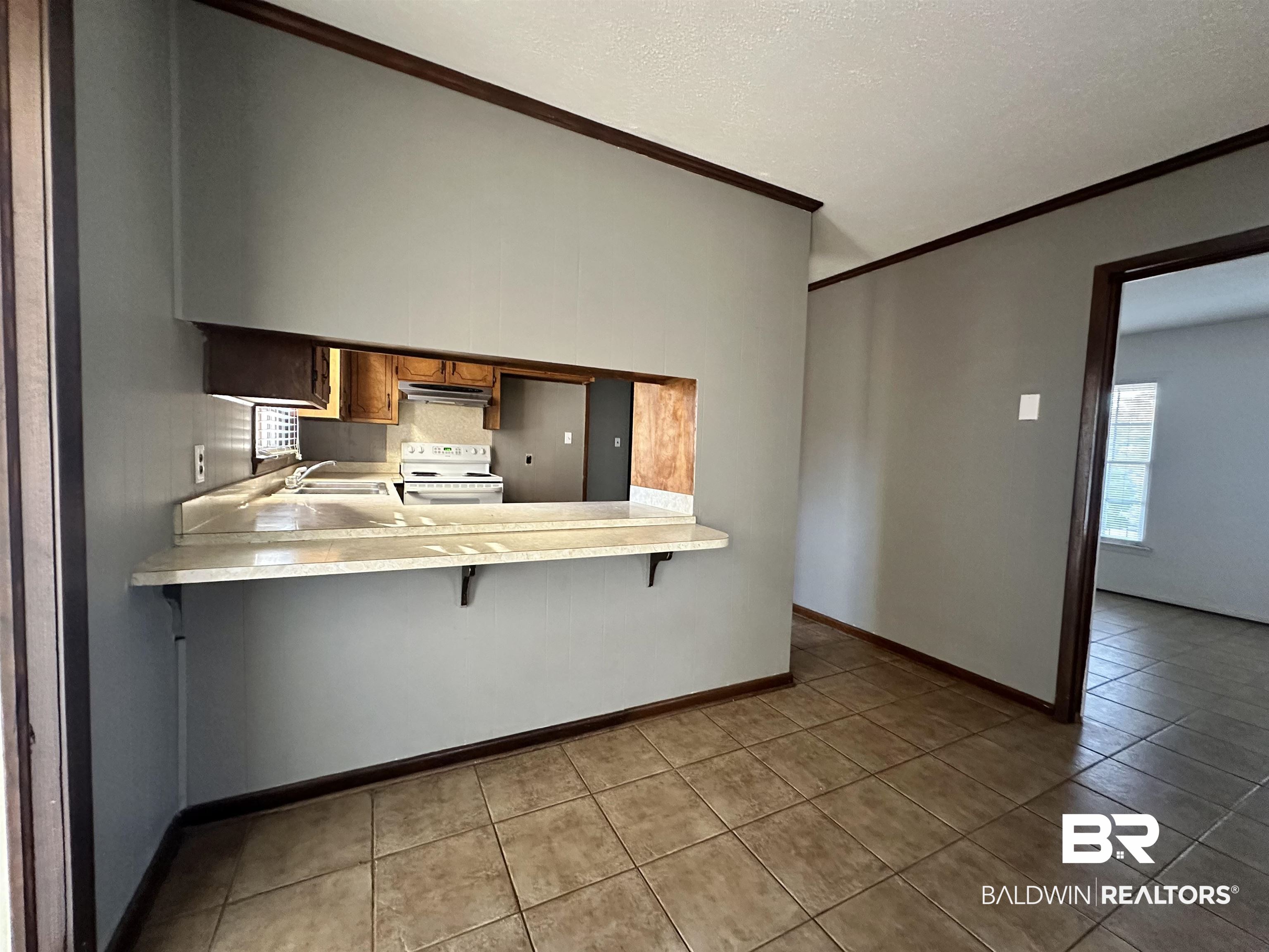 2664 Sowell Road Brewton, AL 36426 - Photo 4 of 12 Kitchen with a kitchen bar, kitchen peninsula, white electric range oven, light tile patterned flooring, and ornamental molding