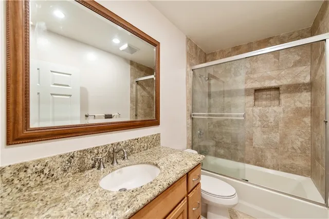 a bathroom with a granite countertop sink toilet mirror and shower