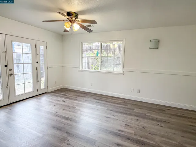 an empty room with wooden floor fan and windows