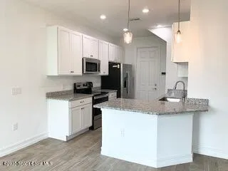 a kitchen with stainless steel appliances granite countertop a sink a stove a refrigerator a microwave oven with white cabinets and wooden floor