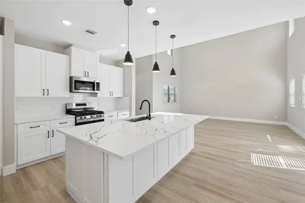 a kitchen with stainless steel appliances a stove a sink a refrigerator a center island a stove and white cabinets with wooden floor