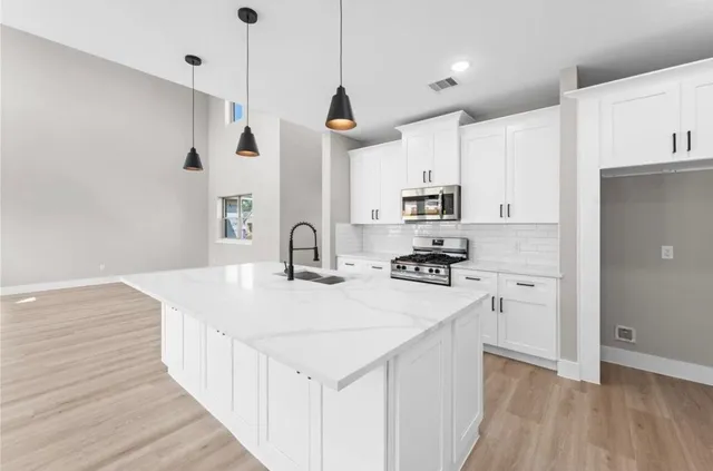 a kitchen with stainless steel appliances granite countertop a sink a stove a refrigerator and white cabinets with wooden floor