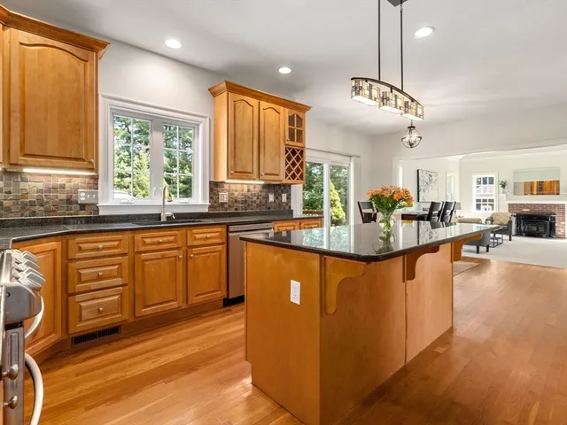 a kitchen with stainless steel appliances granite countertop a refrigerator a sink dishwasher a stove and a dining table with wooden floor