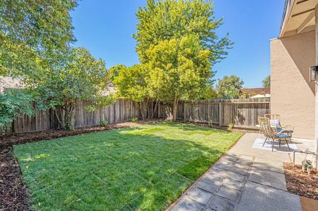 a backyard of a house with table and chairs plants and large tree