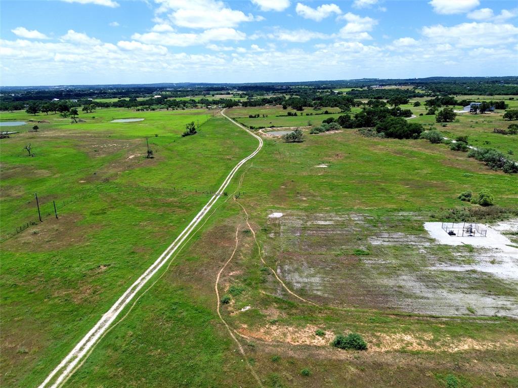 2186 Gilliland Road Springtown, TX 76082 - Photo 18 of 25 Expansive green acreage featuring a defined dirt track, scattered trees, and distant natural water features