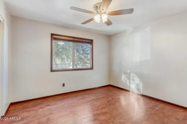 an empty room with wooden floor chandelier fan and windows
