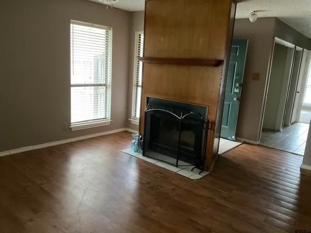 an empty room with wooden floor fireplace and windows