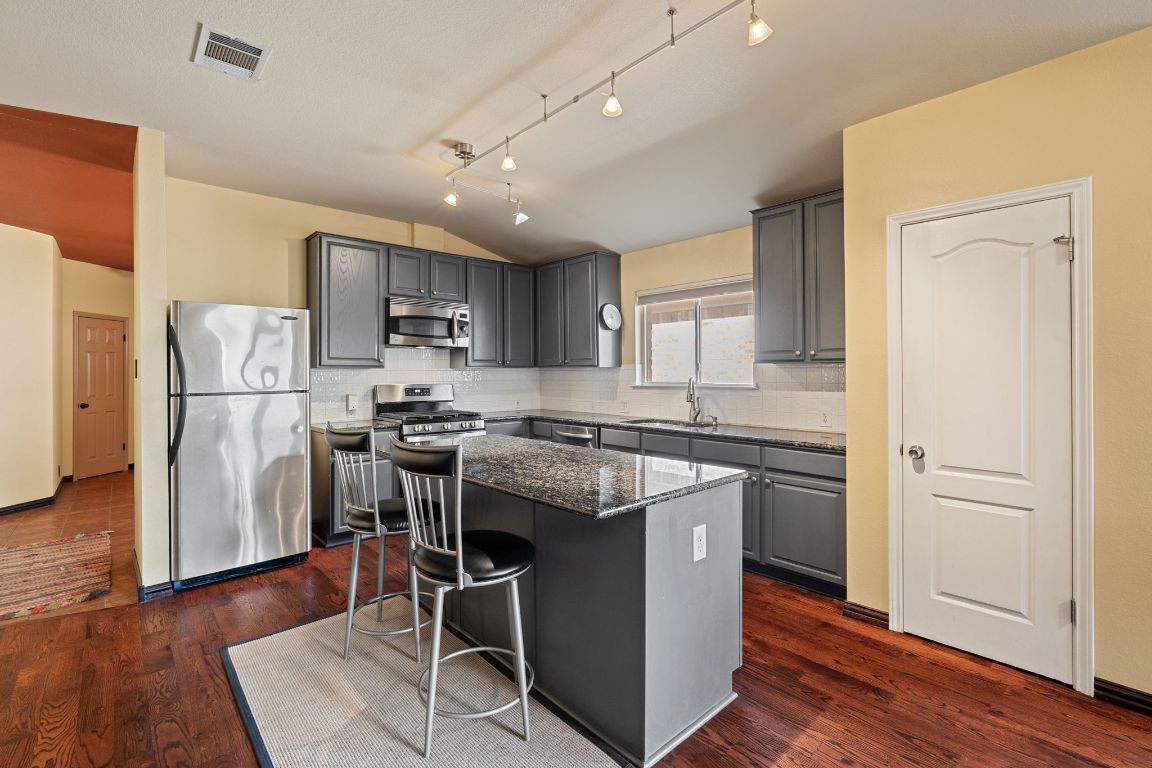 2114 Desco Drive Austin, TX 78748 - Photo 22 of 40 Kitchen featuring appliances with stainless steel finishes, gray cabinetry, lofted ceiling, a sink, and dark stone counters